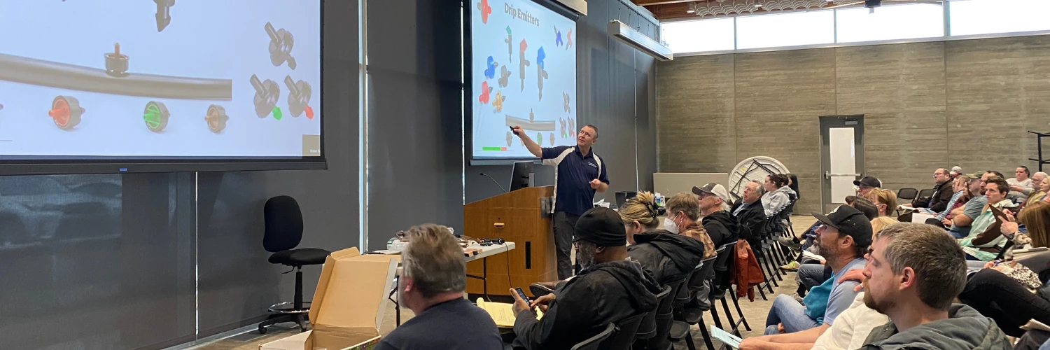 A Weber Basin instructor points to a slide of drip irrigation emitters while a full room of residents watches during a free landscaping class.
